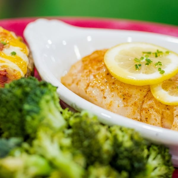 Baked salmon with lemon slices, broccoli, and a loaded baked potato with cheese and bacon.