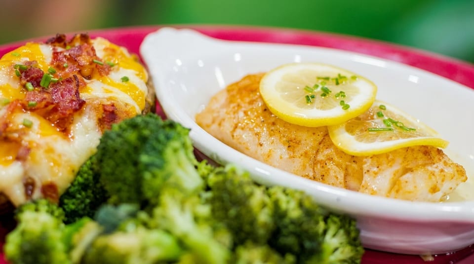Baked salmon with lemon slices, broccoli, and a loaded baked potato with cheese and bacon.