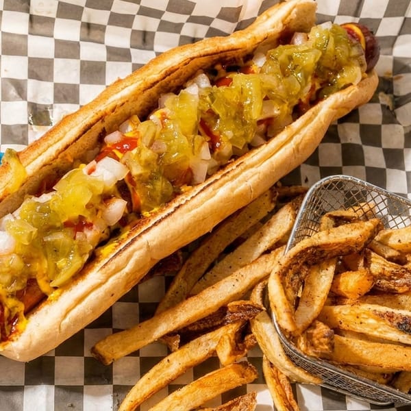 A hot dog with relish, onions, ketchup, and mustard, served with a side of fries.