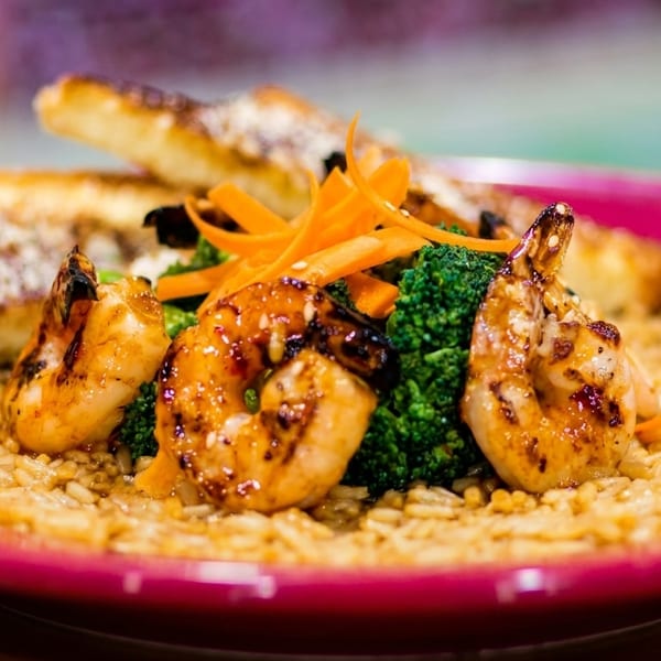 Grilled shrimp with broccoli, carrots, rice, and garlic bread on a red plate.