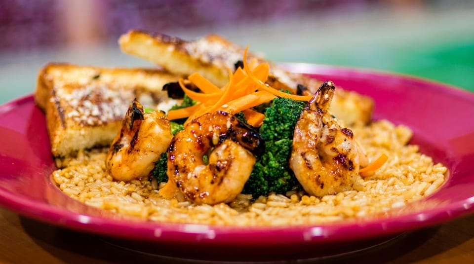 Grilled shrimp with broccoli, carrots, rice, and garlic bread on a red plate.