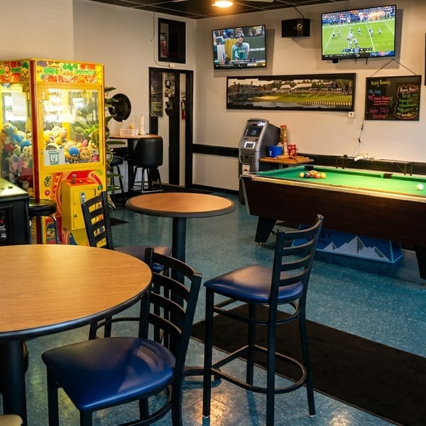 A game room with a pool table, arcade games, high-top tables, and TVs showing sports.